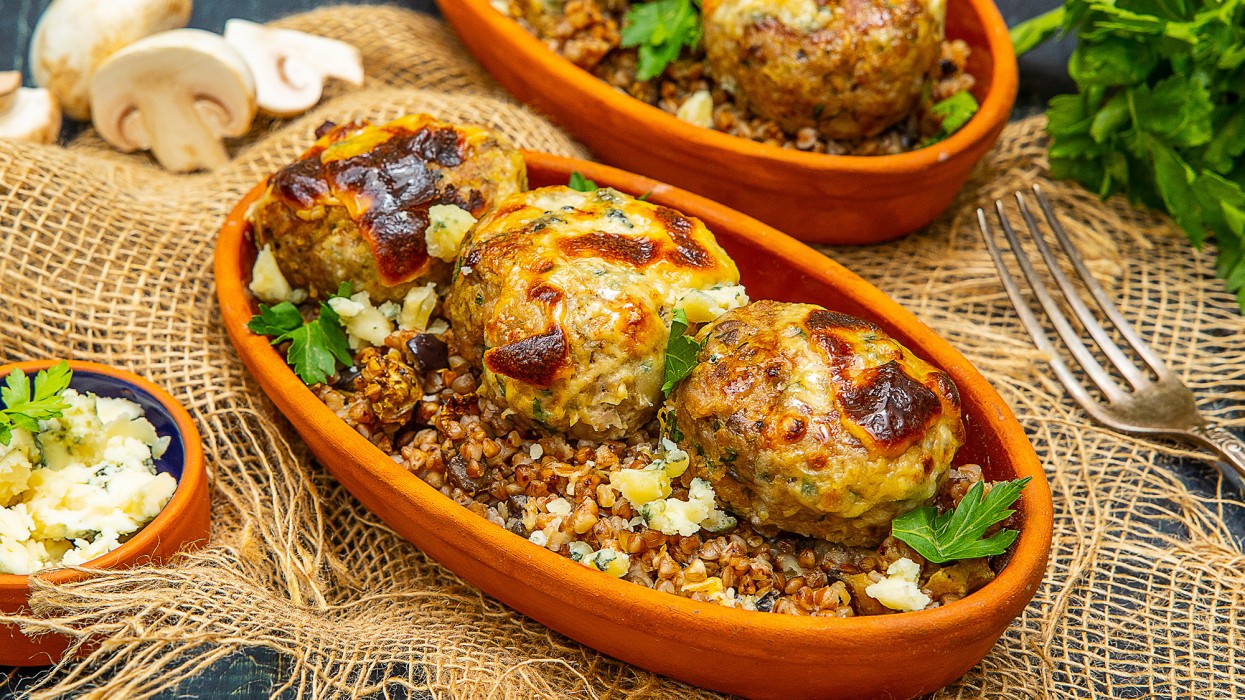 Тефтели по-капитански из свинины с шампиньонами, запечённые на гречневой каше с баклажанами под фирменным сырным соусом с рокфорти и зеленью